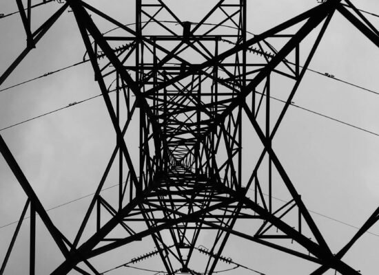 Black and white view from beneath a geometric steel power transmission tower.